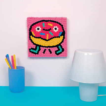 tablou pompom art donut pus pe un perete langa o veioza si un pahar cu carioci colorate - miniLama